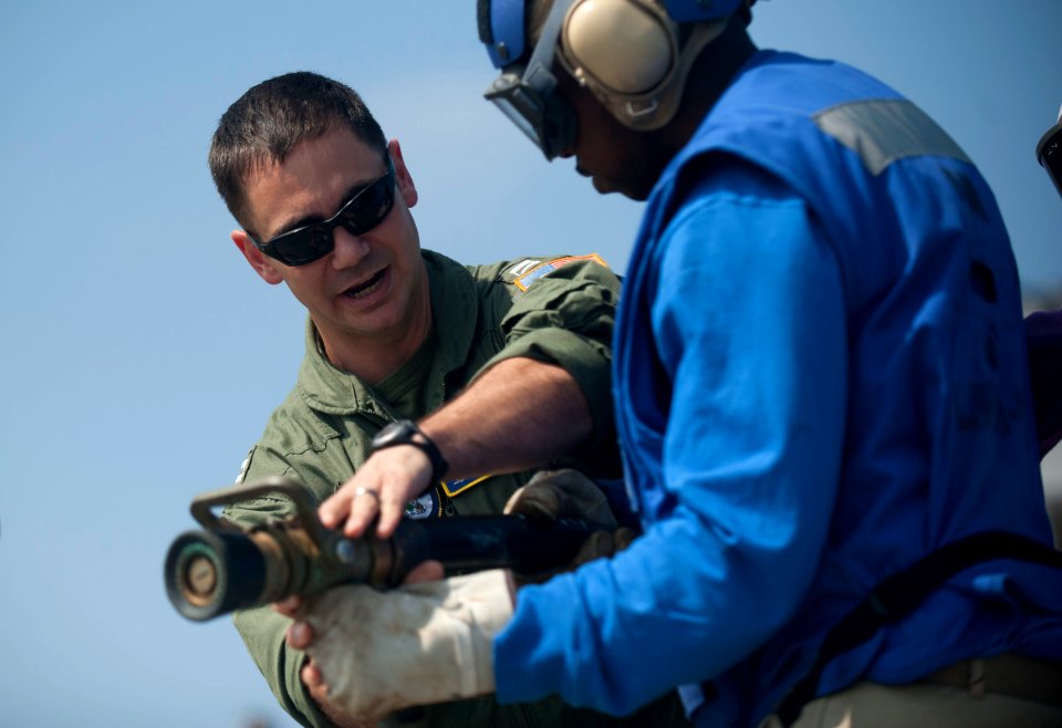 US Navy 120103-N-PB383-541 Lt. Anthony Petrosino explains to a Sailor how to properly man a fire hose during a flight deck firefighting exercise ab