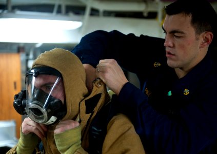 US Navy 120109-N-DR144-061 Chief Machinist's Mate Daniel Pike helps a Sailor don a firefighting ensemble
