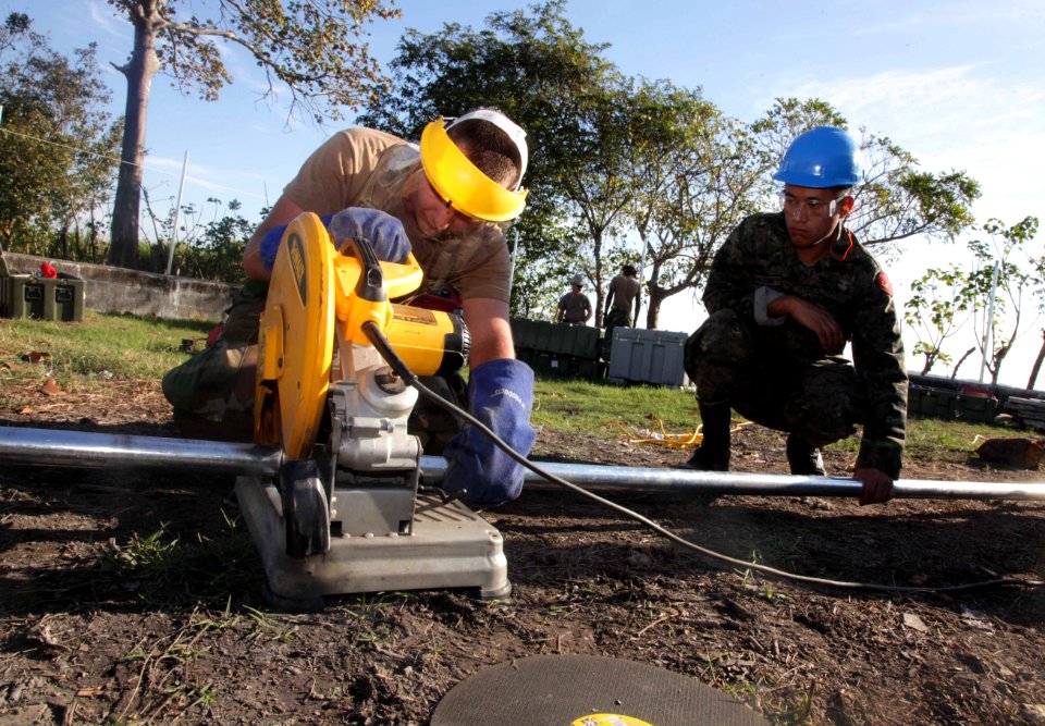 US Navy 120105-A-IP644-033 Equipment Operator 2nd Class Michael McAfee cuts segments of pipe for a fence
