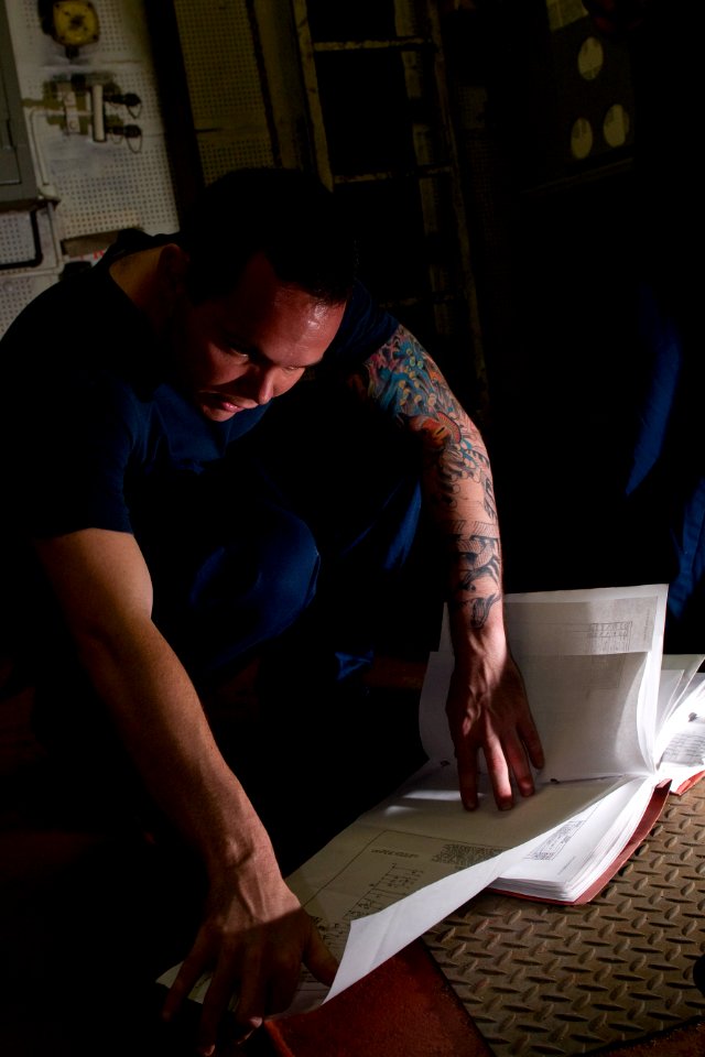 US Navy 120105-N-TZ605-211 Electrician's Mate 3rd Class Joshua Scammell eviews electrical schematics while troubleshooting an air conditioning powe