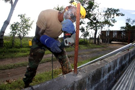 US Navy 120105-A-IP644-103 Construction Electrician Castro Amoakoh shaves the side of a prop for a fence being built at Escuela Rural Aldea Magueye
