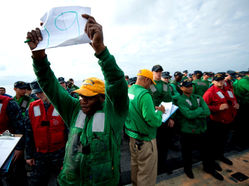 US Navy 120107-N-DR144-100 Aviation Boatswain's Mate (Equipment) 1st Class Earl Hendricks holds up the number of his division's life raft as Sailor