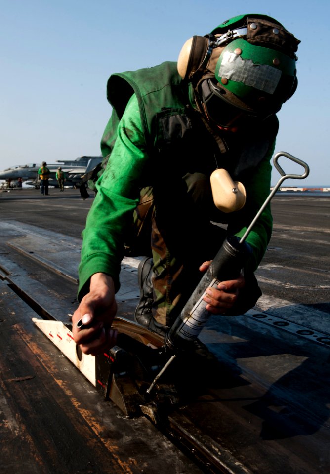 US Navy 120111-N-OY799-065 Aviation Boatswain's Mate (Equipment) Airman Krzysztof Urbanik greases the catapult shuttle on the flight deck of the Ni