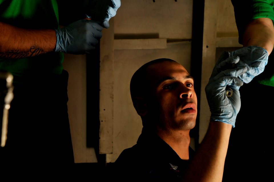 US Navy 120112-N-ZI635-100 A shipmate hands bolts to Aviation Structural Mechanic 2nd Class Christian Samaras as he performs maintenance on the ti