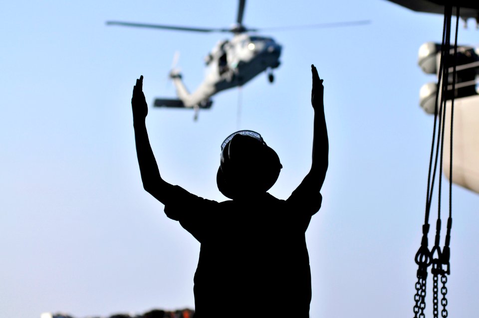US Navy 120113-N-ZI635-342 Boatswain's Mate 3rd Class Charlesa Anderson signals to the Military Sealift Command fast combat support ship USNS Raini