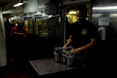 US Navy 120124-N-RG587-077 Aviation Ordnanceman Airman Byron Foster takes clean silverware from the scullery to the chow line aboard the Nimitz-cla