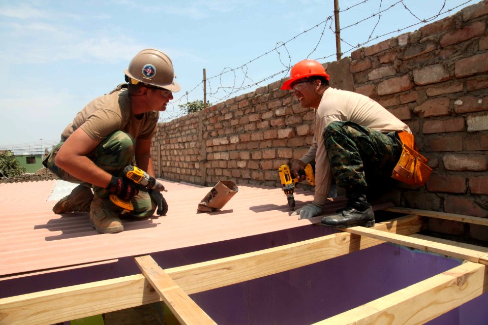US Navy 120127-A-IP644-067 Equipment Operator 2nd Class Michael McAfee and a Peruvian combat engineer attach a roof to a new school