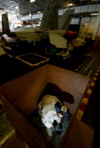 US Navy 120124-N-DR144-388 Airman Recruit Travis Nesbit works inside a cardboard shipping container to control dust and flying debris as he sands o