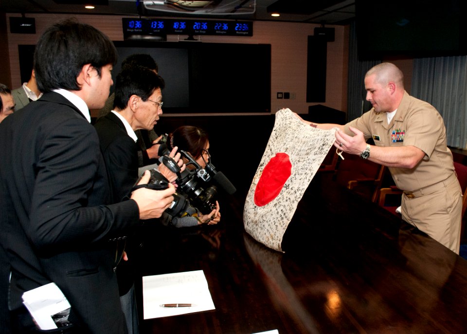 US Navy 120125-N-AG621-015 Lt. j.g. Michael Reid unveils a World War II-era Japanese flag to reporters from the Yokosuka Press Club