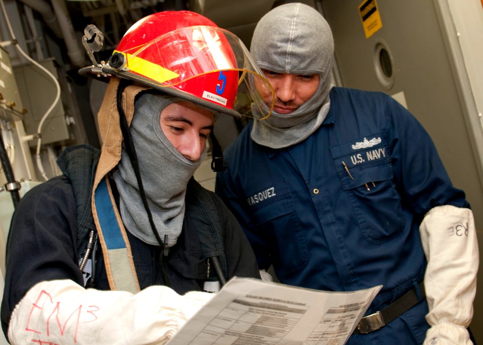US Navy 120127-N-OH194-010 Electrician's Mate 3rd Class Ricardo Torres and Electrician's Mate 2nd Class Vasquez review an electric isolation guide
