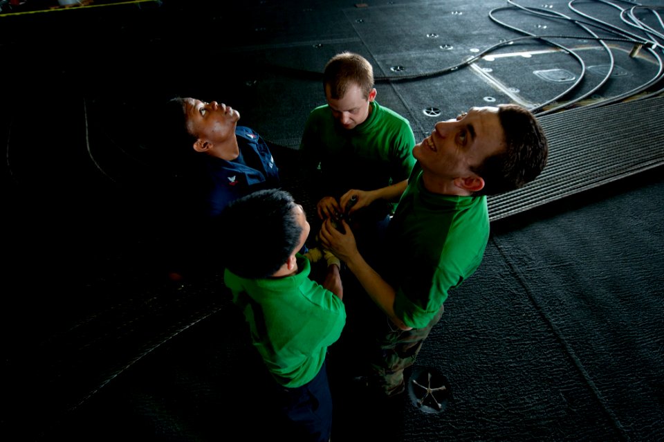 US Navy 120130-N-BT887-391 Sailors check the overhead in the hangar bay for a place to send an arresting gear cable aboard the Nimitz-class aircraf
