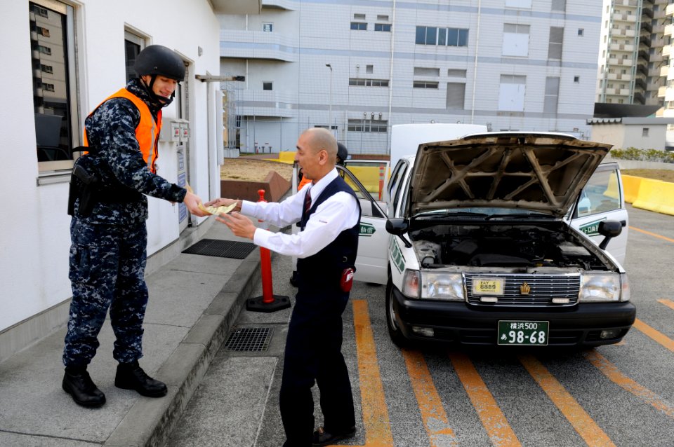 US Navy 120130-N-IO627-028 Hospitalman Derek Sine hands an instruction sheet to a Japanese taxi driver during a vehicle search at a vehicle inspect