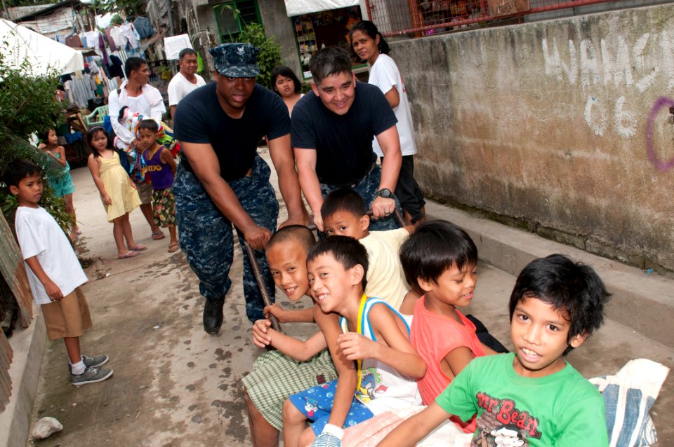 US Navy 120201-N-OH194-080 ire Controlman 2nd Class Kwasi Smith and Chief Hospital Corpsman Jason Juarez play with children during a community serv
