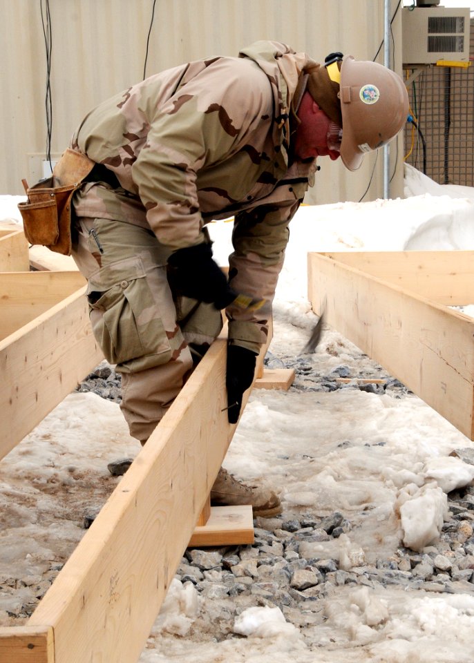 US Navy 120202-N-SD610-001 A Sailor attaches a mud sill to a joist during the construction of wooden flooring for installation in an Alaska tent