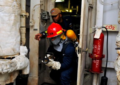 US Navy 120210-N-ZZ999-006 Senior Chief Ship's Serviceman Mario S. Rivers directs Machinist's Mate 3rd Class Mark J. Ligon towards a fire during a