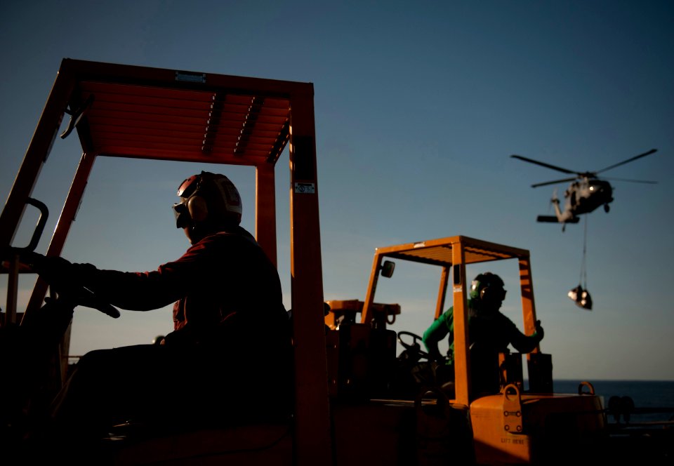 US Navy 120209-N-DR144-516 Sailors moves pallets with forklifts as an MH-60S Sea Hawk helicopter assigned to Helicopter Anti-Submarine Squadron (HS
