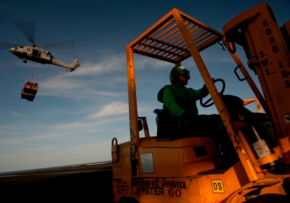 US Navy 120209-N-DR144-430 A supply department Sailor moves pallets with a forklift as an MH-60S Sea Hawk helicopter assigned to Helicopter Anti-Su