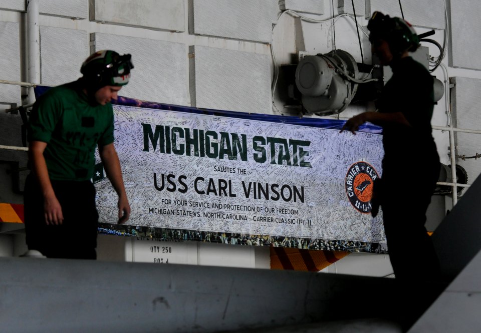 US Navy 120210-N-GZ832-035 Sailors perform maintenance on an F-A 18C Hornet in front of a signed Michigan State banner commemorating the inaugural