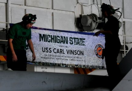 US Navy 120210-N-GZ832-035 Sailors perform maintenance on an F-A 18C Hornet in front of a signed Michigan State banner commemorating the inaugural