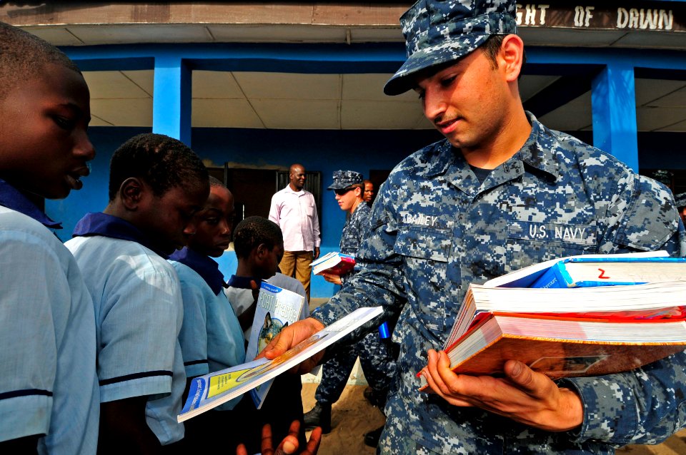 US Navy 120216-N-IZ292-045 Seaman Thomas Bailey, assigned to the guided-missile frigate USS Simpson (FFG 56), hands books to school children from t