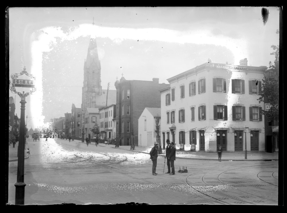 View of 5th Street, N.W., East side, looking North from G Street with two men standing in the street conversing and steeple from St. Mary's Catholic Church can be seen standing high above LCCN2016646844
