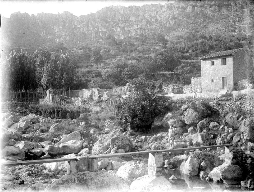 Vista del Brugent amb una casa i una dona creuant per una fusta sobre el riu (AFCEC RIBASV C 2726)