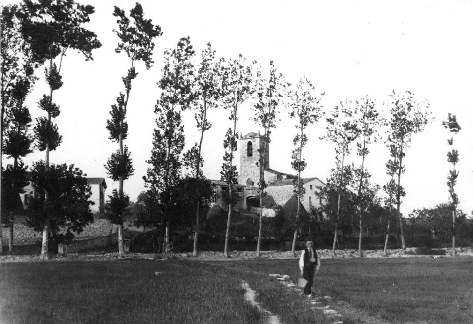 Vista general de l'Església de Santa Maria de Porqueres, en primer terme un home en un prat