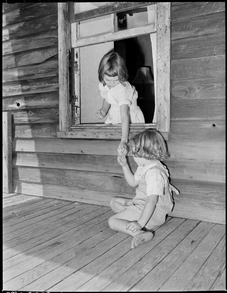 Wanda Lee Sergent hands her sister, Bobbie Jean, an ice cream cone through the window opening from the front porch to... - NARA - 541318