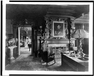 Study with portrait of woman in Elizabethan dress, over fireplace, fringe lamp at right, and buffalo statue on left; elk head on wall and grandfather clock in background, in home of Edmund LCCN94502502