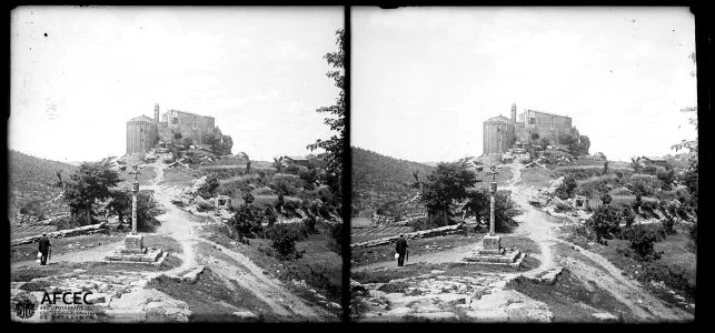 Un home al costat de la creu de terme de Madrona i al fons una casa i l'església vella de Sant Pere