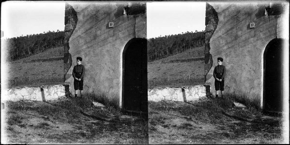 Un nen davant al costat de la porta d'una casa i al fons un bosc