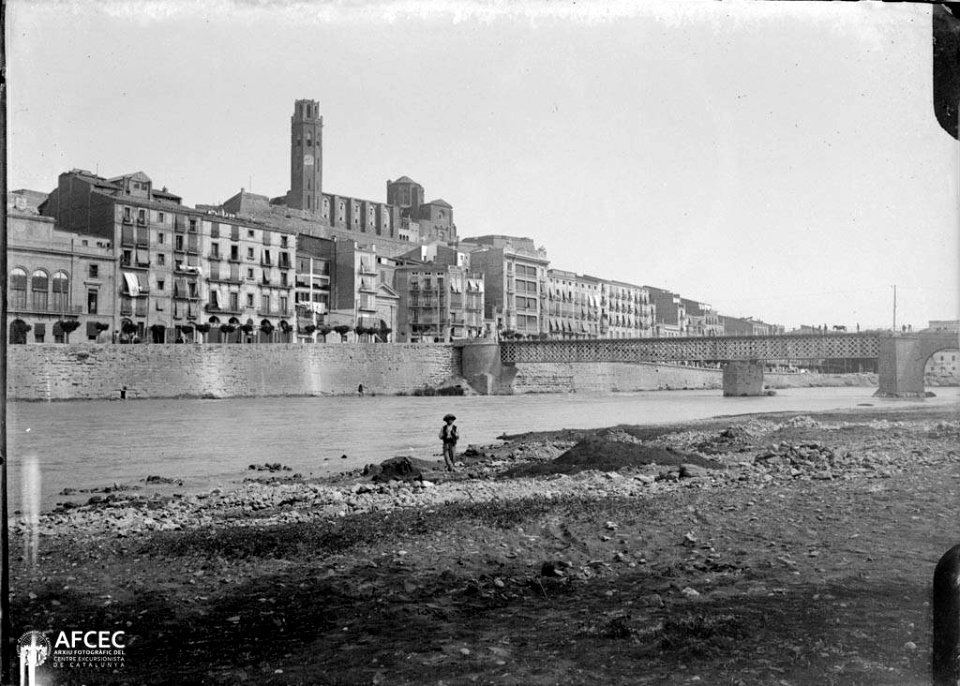Un nen a la riba del riu Segre, més enllà un pont i la ciutat de Lleida