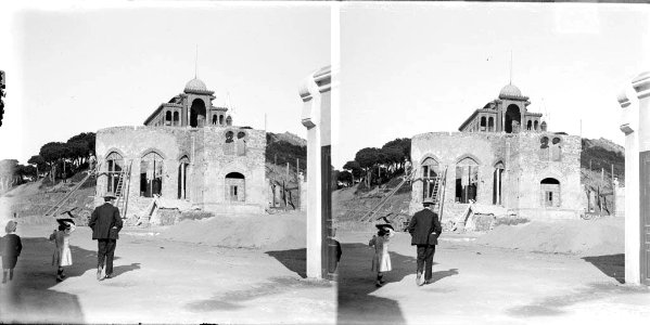 Un home i dos nens al davant d'un edifici en construcció i al fons el pavelló de la Reina