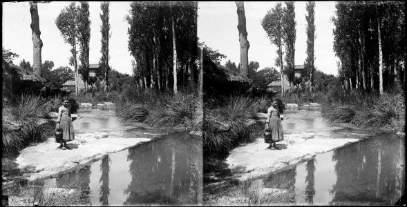Una nena amb un càntir a la vora d'un riu , a la riba arbres i una casa al fons