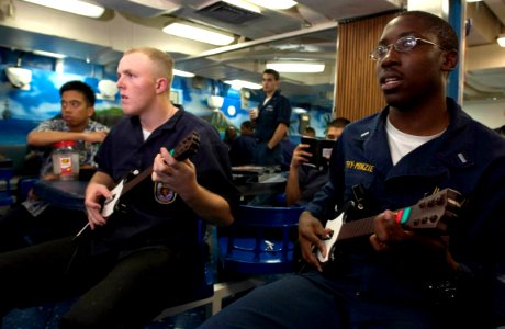 US Navy 060902-N-9851B-011 Culinary Specialist Seaman Damien McCullough, left and Lt J.G. Levy-Minzie play an electric guitar video game on the mess deck of aboard the guided missile destroyer USS Hopper (DDG 70) photo