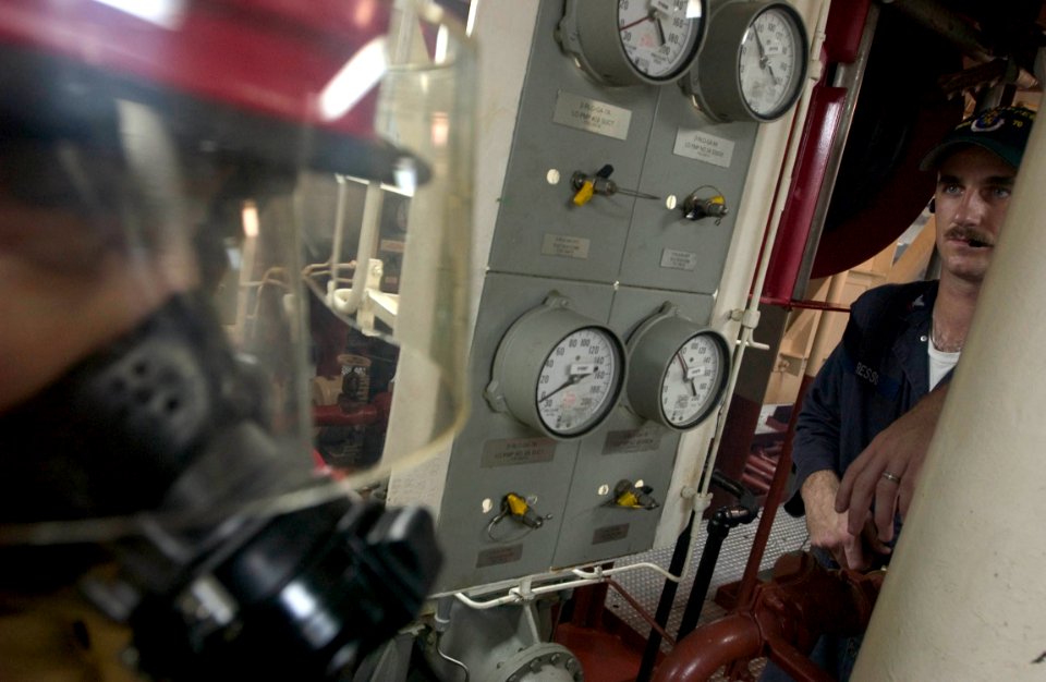 US Navy 060830-N-9851B-003 Engineering Training Team member, Engineman 2nd Class Daniel Resso observes a fire team combating a simulated fire in the number two main Machinery Room aboard the Arleigh Burke-class guided missile