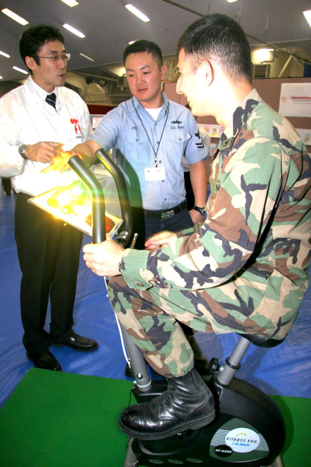 US Navy 061026-N-1113S-003 Petty Officer 2nd Class Mark Somsel generates electricity on a bicycle while Tokyo Electric Power Company's Yasumasa Musha and explain the process during Atsugi's fourth annual Energy Fair