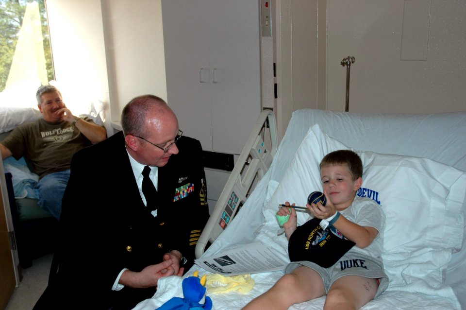 US Navy 061018-N-5531C-002 A chief petty officer assigned to the Virginia-class fast-attack submarine North Carolina (SSN 777) gives a ball cap to a child at Duke Children's Hospital