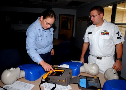 US Navy 061016-N-8544C-001 Hospital Corpsman 2nd class Nicholas Huso instructs Mass Communication Specialist 2nd Class Denise Ordonez how to properly operate an automated external defibrillator (AED)