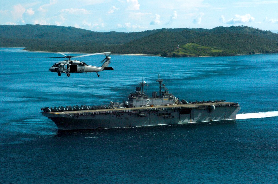 US Navy 061104-N-5067K-076 With a MH-60S Seahawk assigned to the Island Knights of Helicopter Sea Combat Squadron Two Five (HSC-25) flying as a channel guard, USS Essex (LHD 2) passes the Capul Island Lighthouse