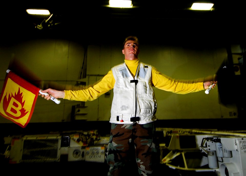 US Navy 061104-N-3729H-121 Aviation Boatswain's Mate 1st Class Michael Feliciano waves red and black flags to represent a fire during a general quarters drill in the hangar bay of nuclear-powered aircraft carrier USS John C. St