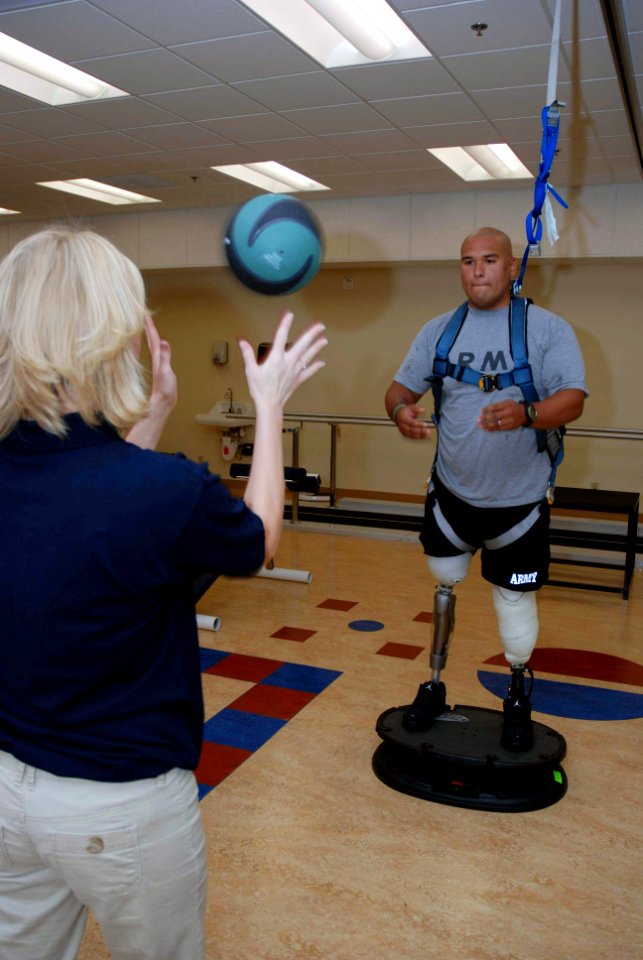 US Navy 071015-N-5086M-002 U.S. Army Spc. Saul Martinez trains with the medicine ball while standing on a balancing tool and using the hands-free harness walking gait-training device during a therapy session