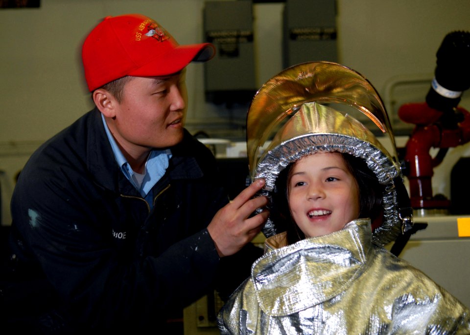 US Navy 071006-N-7981E-131 Aviation Boatswain's Mate (Handling) 3rd Class Woo Choe helps a young girl into a fire suit at a shipboard fire fighting display in the hangar bay of Nimitz-class aircraft carrier USS Abraham Lincoln