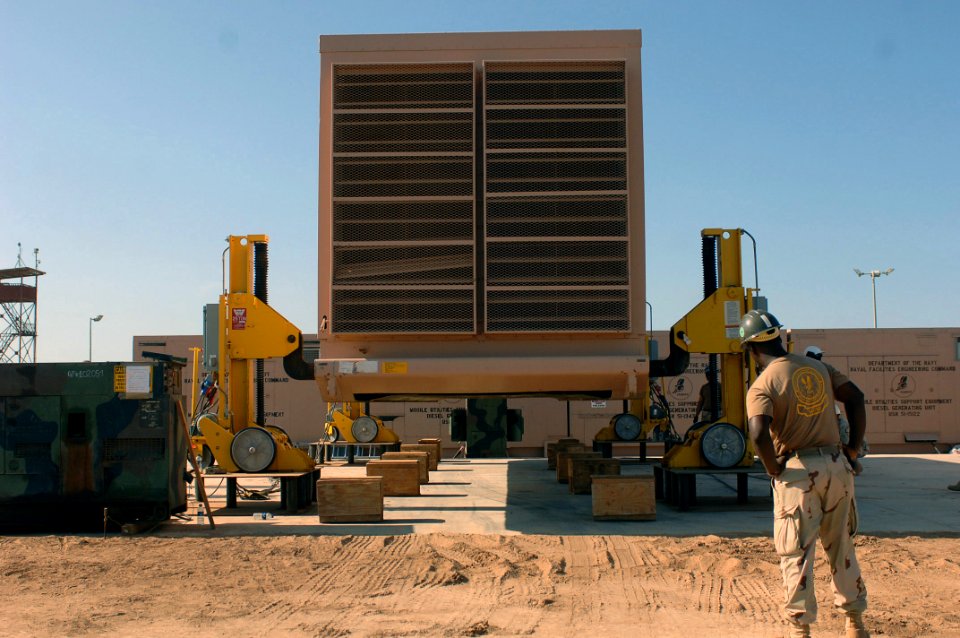 US Navy 071018-N-1003P-034 Construction Mechanic 1st Class Alfredo Ozuna, the lead mechanic attached to Mobile Utilities Support Equipment looks on as a generator container is lowered onto a concrete pad
