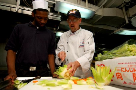 US Navy 071022-N-5387K-007 Chef Ray Duey instructs Culinary Specialist Seaman Keyon Burrell on how to make a vegetable garnish aboard USS Kitty Hawk (CV 63)