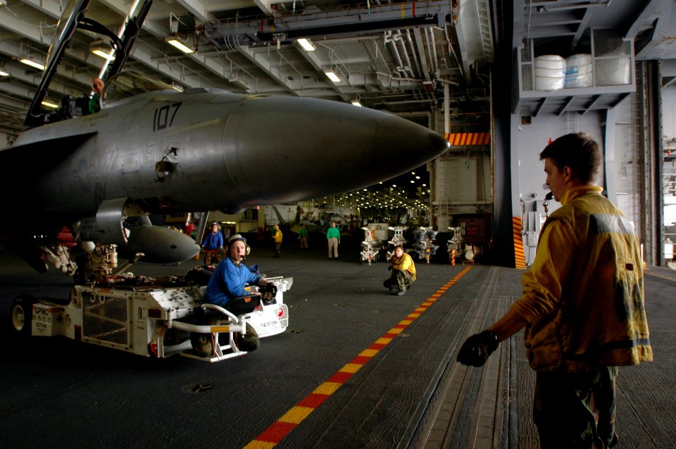 US Navy 071023-N-3946H-043 Aviation Boatswain's Mate (Handling) Airman James Zembower, directs a spotting dolly, as an F-A-18F Super Hornet is parked in the hangar bay of the USS Kitty Hawk (CV 63)