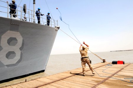 US Navy 090630-N-6814F-057 British Royal Navy Leading Seaman Lee Noak throws a messenger line to the deck of mine countermeasure ship USS Scout (MCM 8) as it pulls into Umm Qasr, Iraq photo