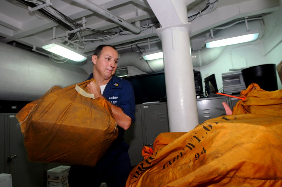 US Navy 090701-N-3610L-053 Postal Clerk 2nd Class Dewayne Mobley throws a bundle of mail on a pile in the post office of the aircraft carrier USS Ronald Reagan (CVN 76)
