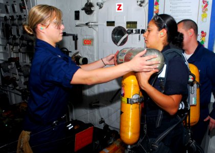 US Navy 090706-N-0515W-017 Damage Controlman 3rd Class Valerie Malloy gives Damage Controlman Fireman Naomi Carrillo self-contained breathing apparatus tanks during a weekly maintenance check of shipboard firefighting equipment