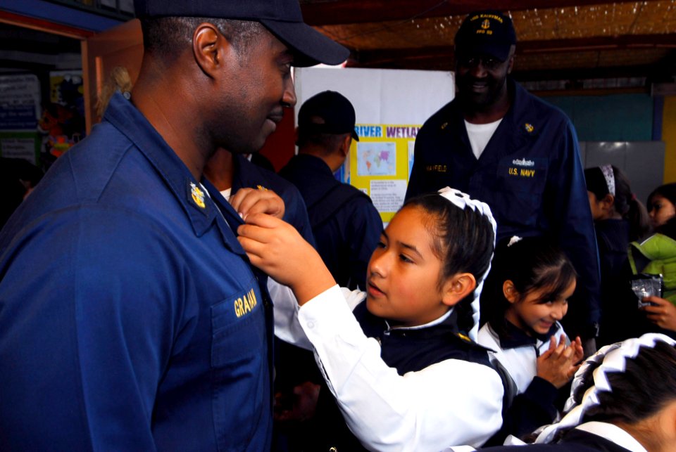 US Navy 090710-N-7092S-110 A student from Escuela General Basica Centenario pins a welcome card to Command Master Chief David Graham from guided-missile frigate USS Kauffman (FFG 59), during a community relations project in Ari
